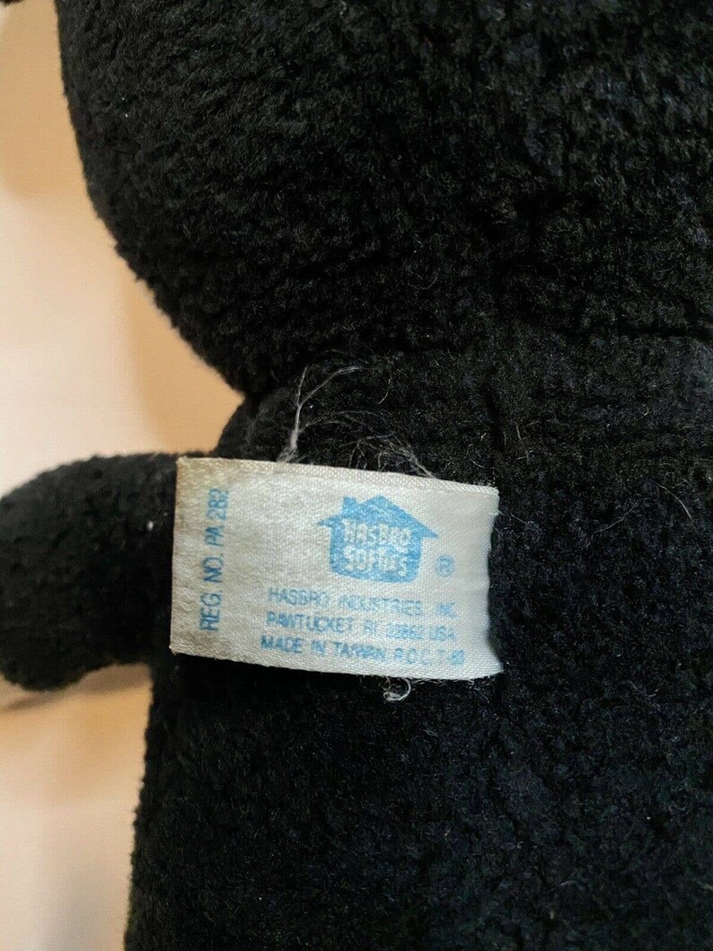 Peut inclure: Gros plan sur un jouet en peluche noir avec une &eacute;tiquette attach&eacute;e. L'&eacute;tiquette indique "HASBRO INDUSTRIES INC PAWTUCKET RI 02862 USA MADE IN TAIWAN R.O.C." Le jouet en peluche a un aspect doux et textur&eacute;.