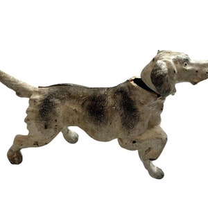 Può includere: Statuetta vintage di cane in ghisa, dipinta di bianco con macchie e accenti neri. Il cane è raffigurato in posizione di corsa, con la coda estesa. La statuetta ha un aspetto invecchiato, che suggerisce età e utilizzo.