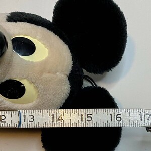 Peut inclure: Une t&ecirc;te de Mickey Mouse en peluche, principalement noire et blanche, avec de grandes oreilles noires et une expression souriante. La t&ecirc;te mesure environ 10 cm de large. Le jouet est doux et moelleux, avec un design de dessin anim&eacute; classique.