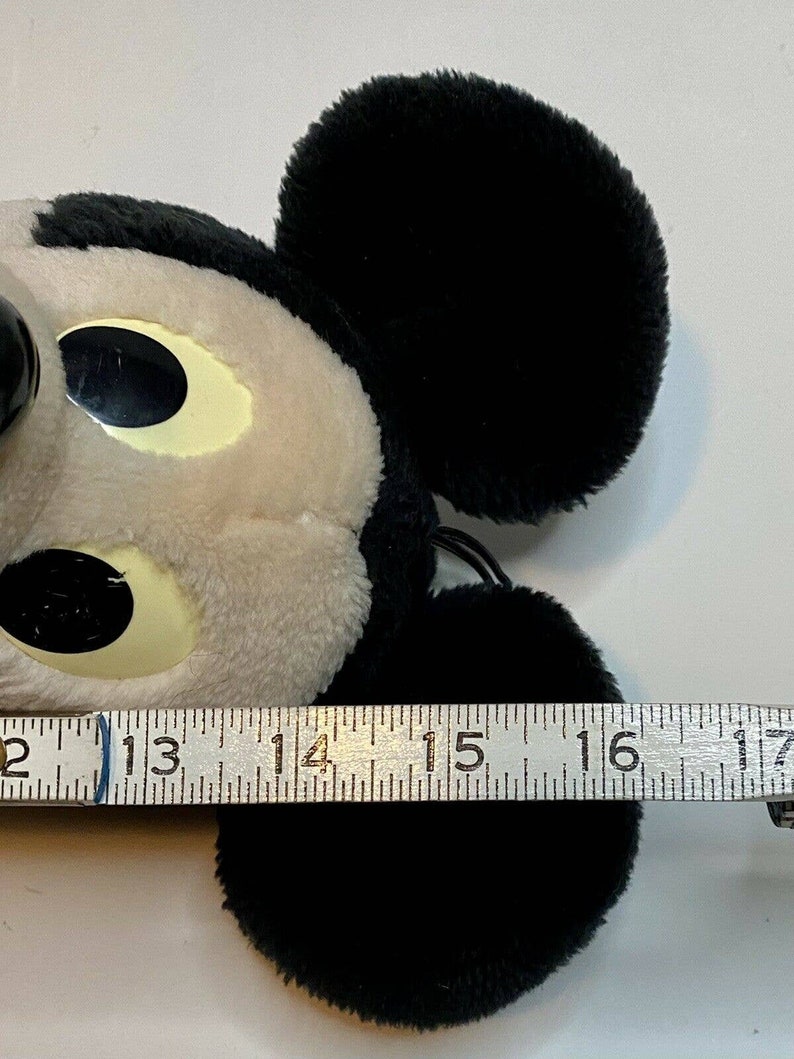 Peut inclure: Une t&ecirc;te de Mickey Mouse en peluche, principalement noire et blanche, avec de grandes oreilles noires et une expression souriante. La t&ecirc;te mesure environ 10 cm de large. Le jouet est doux et moelleux, avec un design de dessin anim&eacute; classique.