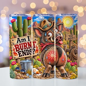 May include: A cylindrical tumbler featuring a desert scene with a cartoon boar wearing a cowboy hat and red bandana. The design includes cacti, a sun, a bucket of ice, sunglasses, and text that reads Am I BURNT ENDS? and TOO HOT! in a desert landscape.