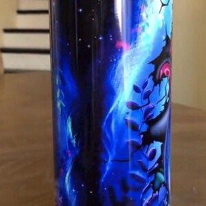 Puede incluir: Un vaso de acero inoxidable con un dise&ntilde;o de galaxia azul y negro. El vaso presenta un cielo nocturno estrellado con una nebulosa giratoria y una silueta de &aacute;rbol.