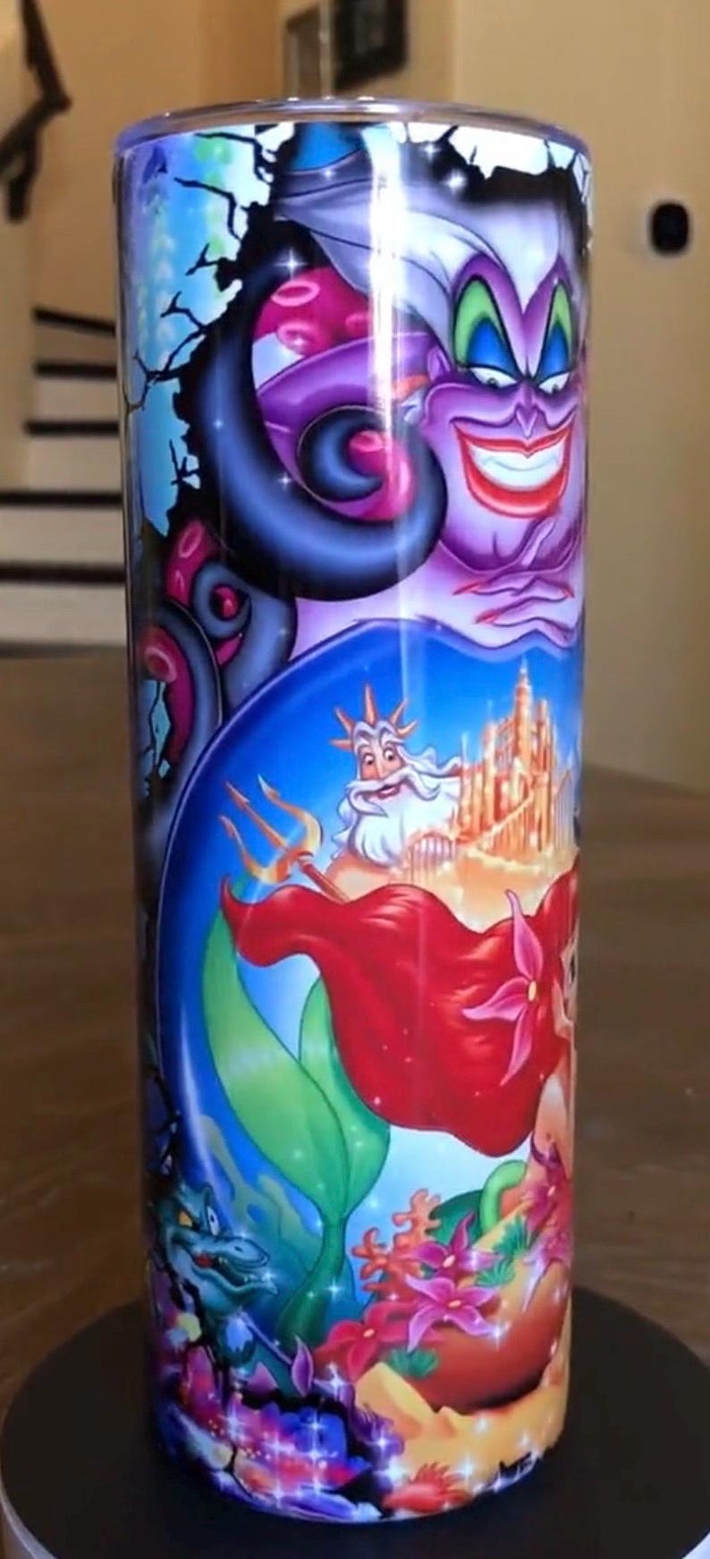 Puede incluir: Un vaso de acero inoxidable colorido con un gr&aacute;fico de &Uacute;rsula, Ariel y el rey Trit&oacute;n de la pel&iacute;cula de Disney La Sirenita. El vaso presenta una gama de colores azul, verde, morado y rojo.