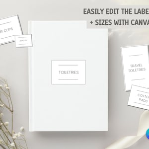 Op de afbeelding: Een wit notitieboek met het woord "TOILETRIES" op de kaft, vergezeld van labels voor "HAIR CLIPS", "JEWELRY", "TRAVEL TOILETRIES" en "COTTON PADS". De tekst "EASILY EDIT THE LABELS + SIZES WITH CANVA" is ook zichtbaar.