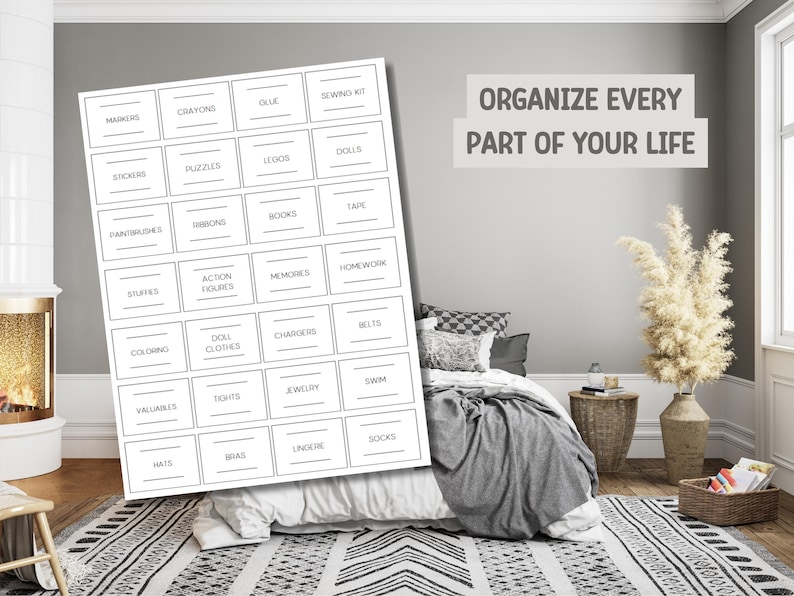 Op de afbeelding: Een witte labelorganizer met diverse opslagcategorie&euml;n, waaronder "Markers", "Crayons" en "Legos". De tekst "Organize Every Part of Your Life" wordt weergegeven boven een bed met een grijze deken en een patroonkleed.