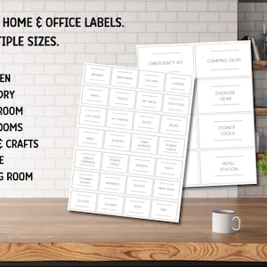 Op de afbeelding: Twee vellen witte etiketten met zwarte tekst voor thuis- en kantoororganisatie. Labels bevatten categorie&euml;n zoals Keuken, Wasserij en Badkamer. De afbeelding toont ook een mok en een kleine plant in een witte pot.