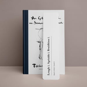 Può includere: Un segnalibro bianco con testo nero che recita "Leugh i. Sgriobh i. Bruidhinn i. Read it. Write it. Speak it." e il testo "Tearlac" in corsivo. Il segnalibro è inserito in un libro con una copertina bianca e una spina dorsale blu.