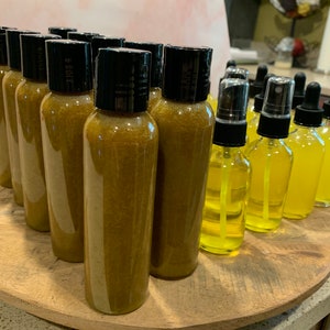 May include: A collection of amber-colored glass bottles with black lids, some with a spray nozzle, arranged on a wooden surface. The bottles contain a liquid that appears to be a golden yellow color.