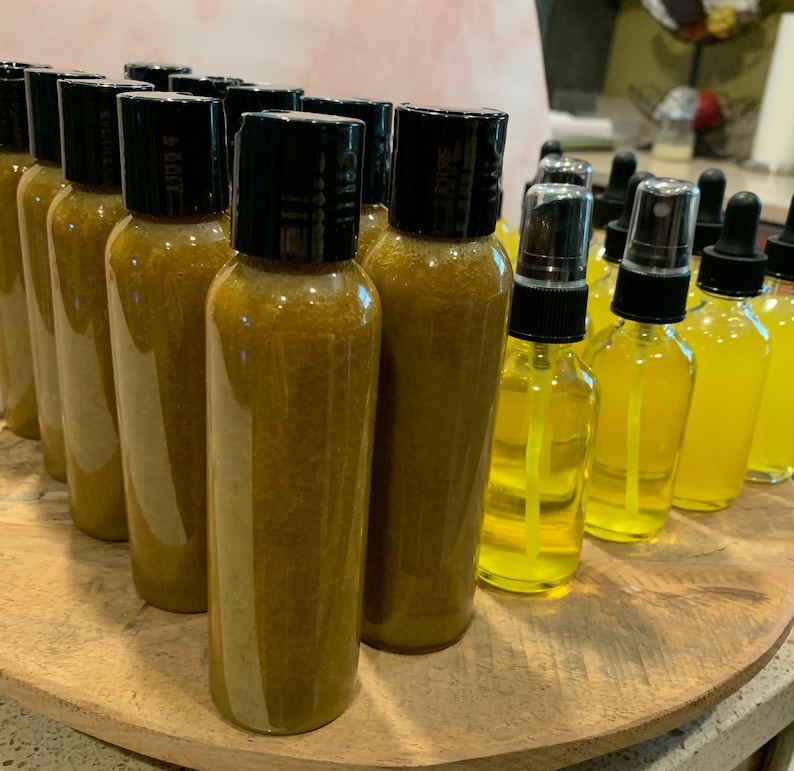 May include: A collection of amber-colored glass bottles with black lids, some with a spray nozzle, arranged on a wooden surface. The bottles contain a liquid that appears to be a golden yellow color.