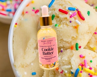 Op de afbeelding: Een klein glazen flesje met geparfumeerde lichaams olie met een gouden dop en druppelaar. Het etiket vermeldt "ROSY POSY Skin & Beauty SCENTED BODY OIL Cookie Butter INGREDIENTS: Sweet almond oil and scented essential oil 1 OZ."
