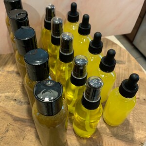 May include: A collection of 14 amber glass bottles with black caps and droppers. The bottles are filled with a yellow liquid. The bottles are arranged in a circular pattern on a wooden surface.