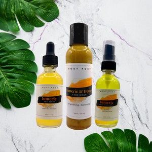 May include: Three glass bottles of turmeric face care products. The bottles are labeled "tumeric face serum", "tumeric & honey face wash", and "tumeric face toner spray".