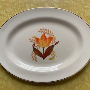 Könnte beinhalten: Weiße ovale Servierplatte mit goldfarbenem Rand und einem gemalten orangefarbenen und braunen Tulpenmotiv.