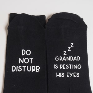 May include: A pair of black socks with white text. One sock says "Do Not Disturb" and the other sock says "ZZz Grandad is resting his eyes".