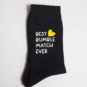 May include: Black socks with a white graphic that says "Best Bumble Match Ever" and a yellow heart.