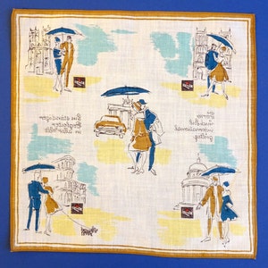 Pu&ograve; includere: Un fazzoletto di lino bianco con un design blu e giallo. Il design presenta coppie che camminano sotto gli ombrelli, un'auto e degli edifici. Il testo "In the shelter of an umbrella" &egrave; stampato sul fazzoletto.