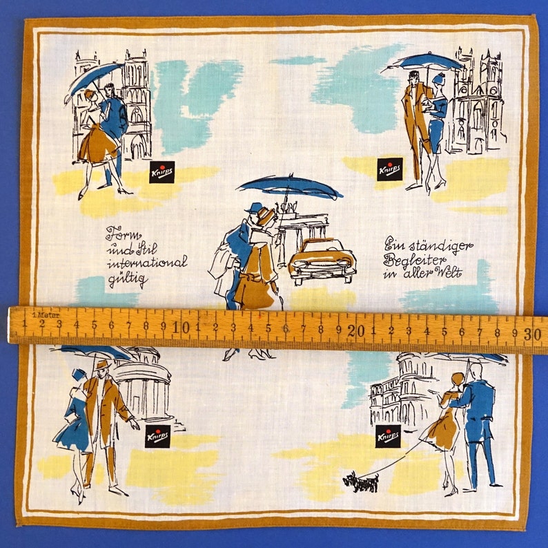 Pu&ograve; includere: Un fazzoletto di cotone bianco con un bordo marrone presenta un motivo ripetuto di coppie che camminano sotto gli ombrelli in vari paesaggi urbani. Il testo "Form und Stil international g&uuml;ltig" e "Ein st&auml;ndiger Begleiter in aller Welt" &egrave; stampato sul fazzoletto.