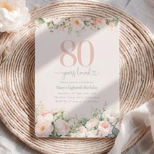 Puede incluir: Una tarjeta de invitación de cumpleaños rectangular con el texto grande en rosa 80 years loved, seguido de los detalles para el octogésimo cumpleaños de Mary el sábado 18 de julio de 2026. La tarjeta tiene ilustraciones de peonías rosas y blancas.