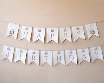 May include: A white banner spelling out "HAPPY BIRTHDAY" in rose-coloured letters. Each pennant features a crown illustration. The banner is strung on a thin, light-coloured string, ideal for a birthday party.