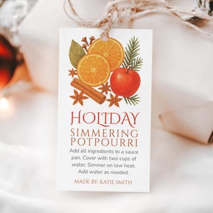 May include: A white tag with the words "HOLIDAY SIMMERING POTPOURRI" and instructions. The tag features illustrations of orange slices, an apple, cinnamon, and star anise. The tag is tied with twine.