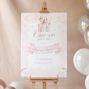 Könnte beinhalten: Ein rosa-goldenes Geburtstagschild auf einer Staffelei. Das Schild zeigt eine Schlossillustration, den Text "One-ce upon a time" und "Princess Sophia's" in Schreibschrift. Das Schild enthält auch den Text "1. Geburtstag" und das Datum.