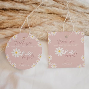 Può includere: Due etichette regalo rosa con accenti di margherita e la scritta "Thank you for making my party" e "one derful!" con il nome "Amelia". Un'etichetta è rotonda, l'altra quadrata, entrambe con spago.