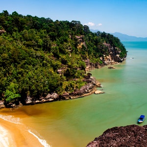 May include: A view from a cliff overlooking a narrow inlet of turquoise water. Lush green foliage covers the cliffs on the left side of the image. A small boat is visible in the water.