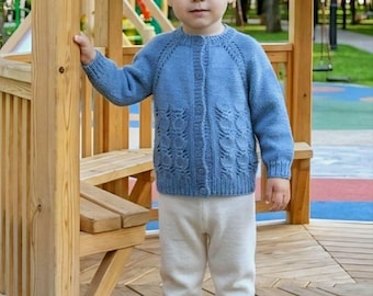 May include: A blue long-sleeved knit cardigan featuring a button-down front and a textured leaf-like pattern on the lower panels, paired with plain off-white knit trousers and white sneakers with hook-and-loop closures.