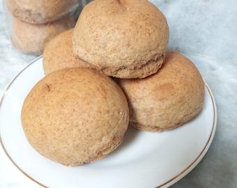 May include: Four brown wheat bread rolls on a white plate with a gold rim. The rolls are round and have a slightly rough texture.