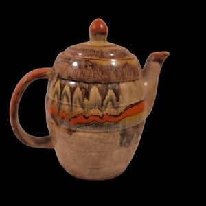 May include: A brown ceramic teapot with a red, orange, and yellow glaze. The teapot has a rounded body and a small spout.