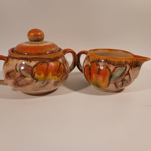 May include: A vintage ceramic sugar and creamer set with a brown, orange, and yellow floral design.