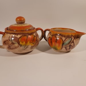 May include: A vintage ceramic sugar and creamer set with a brown, orange, and yellow floral design.