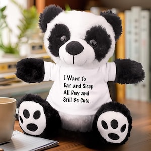 May include: A black and white plush panda bear wearing a white t-shirt with the text "I Want To Eat and Sleep All Day and Still Be Cute".