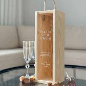 May include: A wooden box with a rope handle, engraved with the text "Father of the Groom". The box has a message inside that says "Thank you for all of your love and support. Love, Zach & Jessica 3.1.2023".