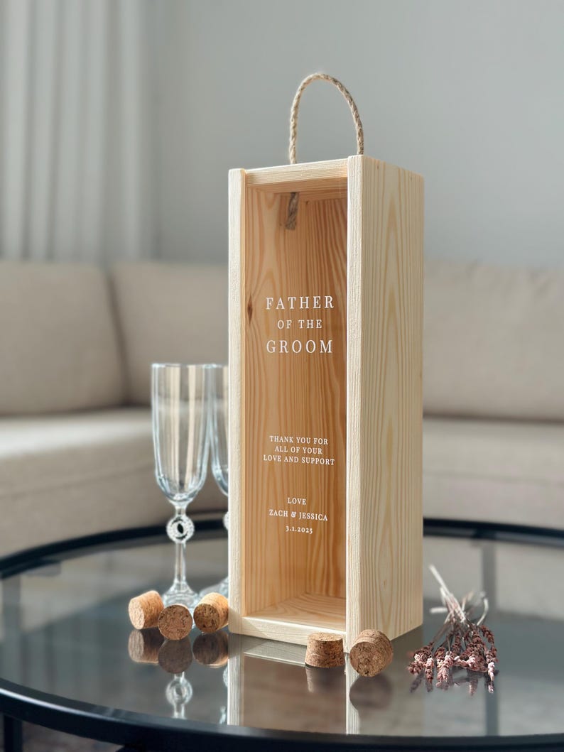 May include: A wooden box with a rope handle, engraved with the text "Father of the Groom". The box has a message inside that says "Thank you for all of your love and support. Love, Zach & Jessica 3.1.2023".