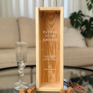 May include: Wooden box with a rope handle, designed for a bottle of wine. The box is engraved with the text "Father of the Groom", a message of thanks, and the names "Zach & Jessica" with a date.