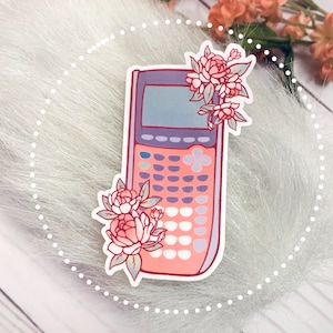 May include: A pink and purple calculator sticker with floral accents. The calculator has a screen, buttons, and a pink and purple colour scheme. The flowers are pink and white.