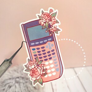 May include: A pink and purple calculator sticker with a floral design. The calculator has a screen, buttons, and a pink and purple color scheme. The flowers are pink and white with green leaves.