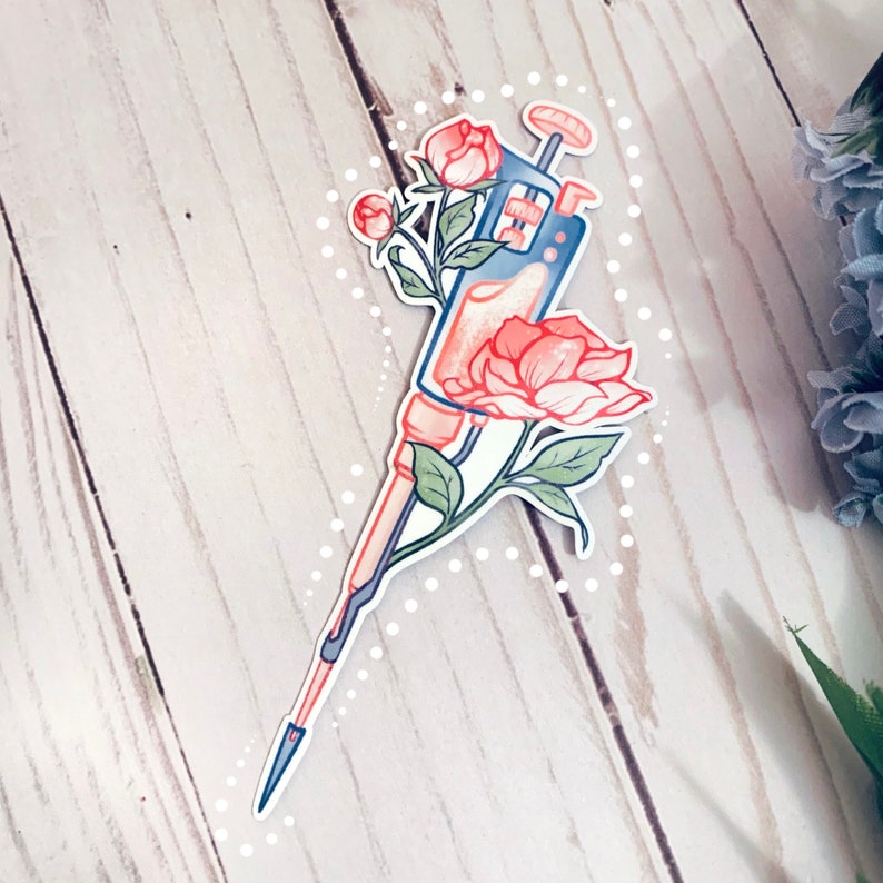 May include: A blue and white pipette with a clear liquid inside, surrounded by pink flowers with green leaves. The pipette is decorated with a white dotted pattern.