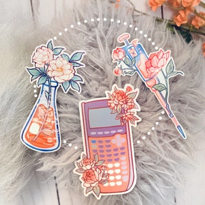 May include: Four stickers featuring floral designs and science-themed imagery. The stickers include a beaker with flowers, a calculator with flowers, a pipette with flowers, and a test tube with flowers. The stickers are on a fuzzy gray background.