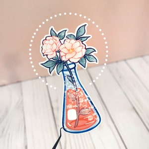 May include: A sticker of a white beaker with a pink flower stem inside. The beaker has markings for 250 ml, 150 ml, 100 ml, and 50 ml. The flower has two pink flowers and green leaves. The sticker is surrounded by a white dotted circle.