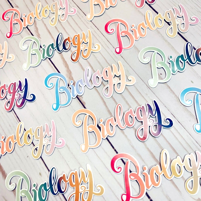 May include: A collection of colourful stickers with the word "Biology" written in a cursive font. The stickers are arranged on a white wooden surface.