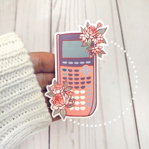 May include: A pink and purple calculator sticker with a floral design. The calculator has a screen and a keypad with buttons. The flowers are pink and white.