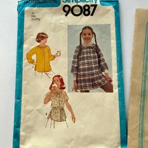 Peut inclure: Patron de couture Simplicity vintage 9087 pour vêtements de filles. L'enveloppe bleue et blanche présente des illustrations de trois tenues différentes. Le texte "Simplicity 9087" est bien en évidence.