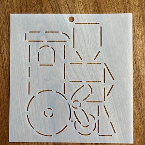 May include: A white plastic stencil with a design of a train engine. The stencil has a hole in the top for hanging.