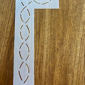 May include: White plastic quilting template with a cut-out design of a continuous chain of ovals. The template is shaped like a right angle.