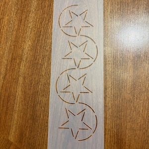 May include: A white plastic stencil with a repeating pattern of five-pointed stars in circles. The stencil is designed for quilting or other crafts.