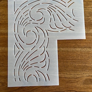 May include: A stencil with a decorative, flowing design. The stencil is made of a translucent, off-white material and features a series of curved lines and shapes. The design is cut out, creating negative space. The stencil has a small hole at the top and the number "#658" printed on it.