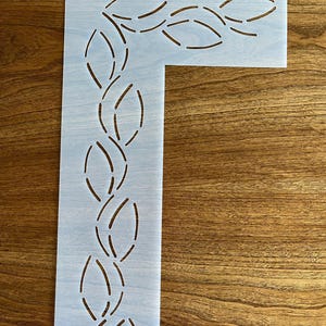 May include: White plastic quilting stencil with a design of a repeating pattern of curved lines and ovals. The stencil has a small hole in the top corner.