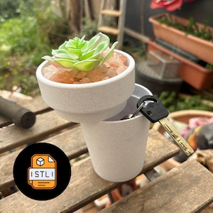 May include: A small, light-colored ceramic planter with a succulent plant and decorative stones. A key is placed in a matching ceramic cup. The image also includes a logo with the text "ISTLI".